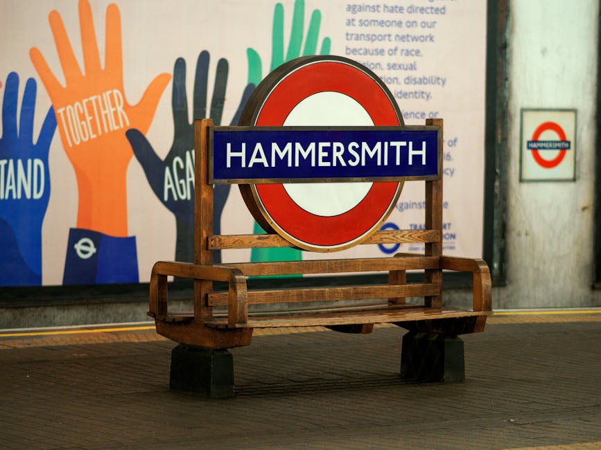 A red double-decker bus displaying the route number 9 and destination Hammersmith is traveling down a busy city street lined with historic buildings. In the foreground, a black lamppost decorated with